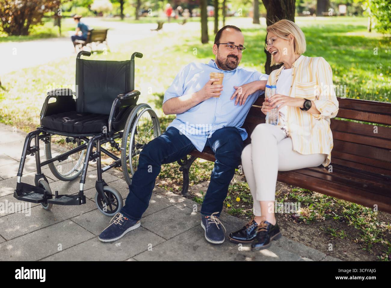 Man in wheelchair is spending time with his mother in park. Paraplegic man is talking with woman. Stock Photo