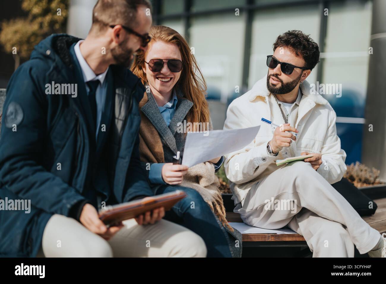 Three professionals collaborating and discussing documents while sitting outside Stock Photo