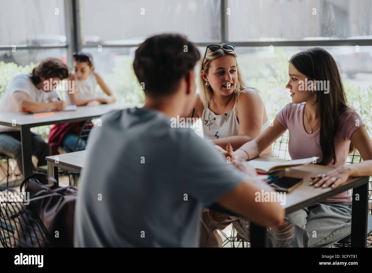 Diverse students collaborating at a study table with open notebooks Stock Photo