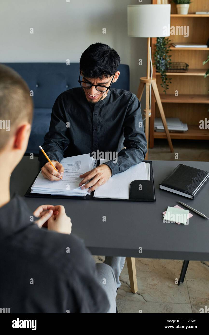 Vertical high angle shot of unrecognizable stylish young woman with short hair sitting in front of joyful HR manager talking about her work experience Stock Photo