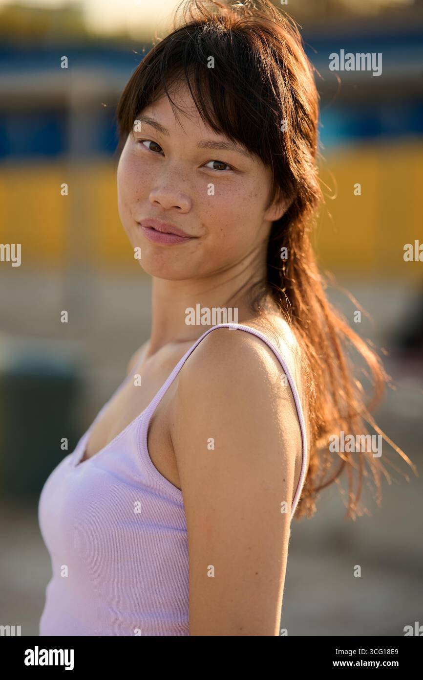 Young asian woman smiling outdoors, enjoying golden hour light Stock Photo