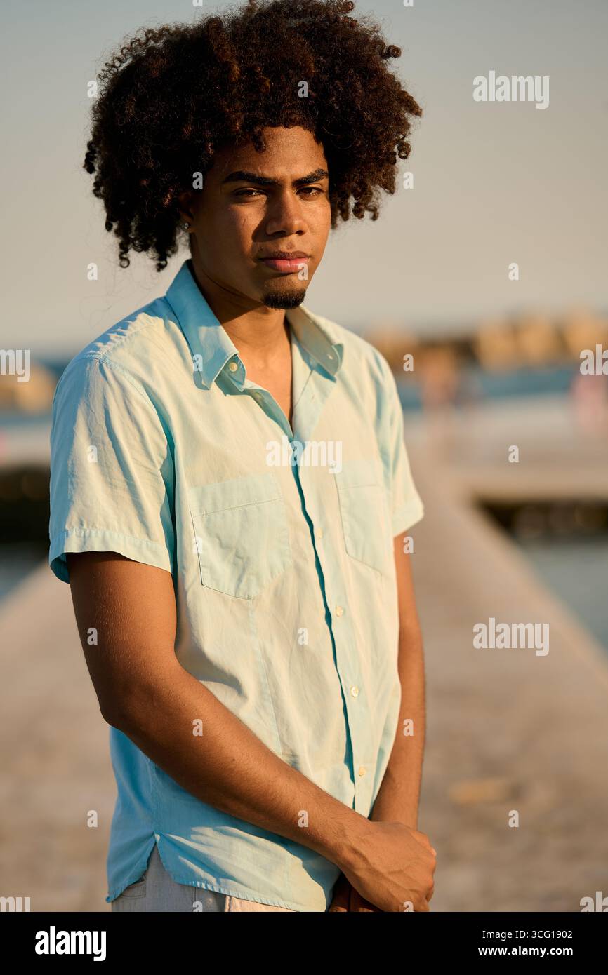 Young man with afro hair posing on pier at sunset Stock Photo