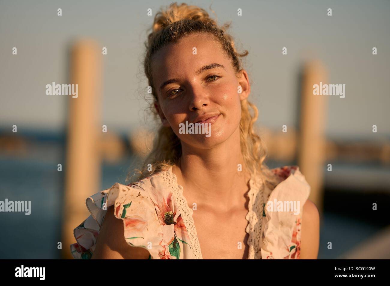 Blonde woman smiling at golden hour by the sea Stock Photo