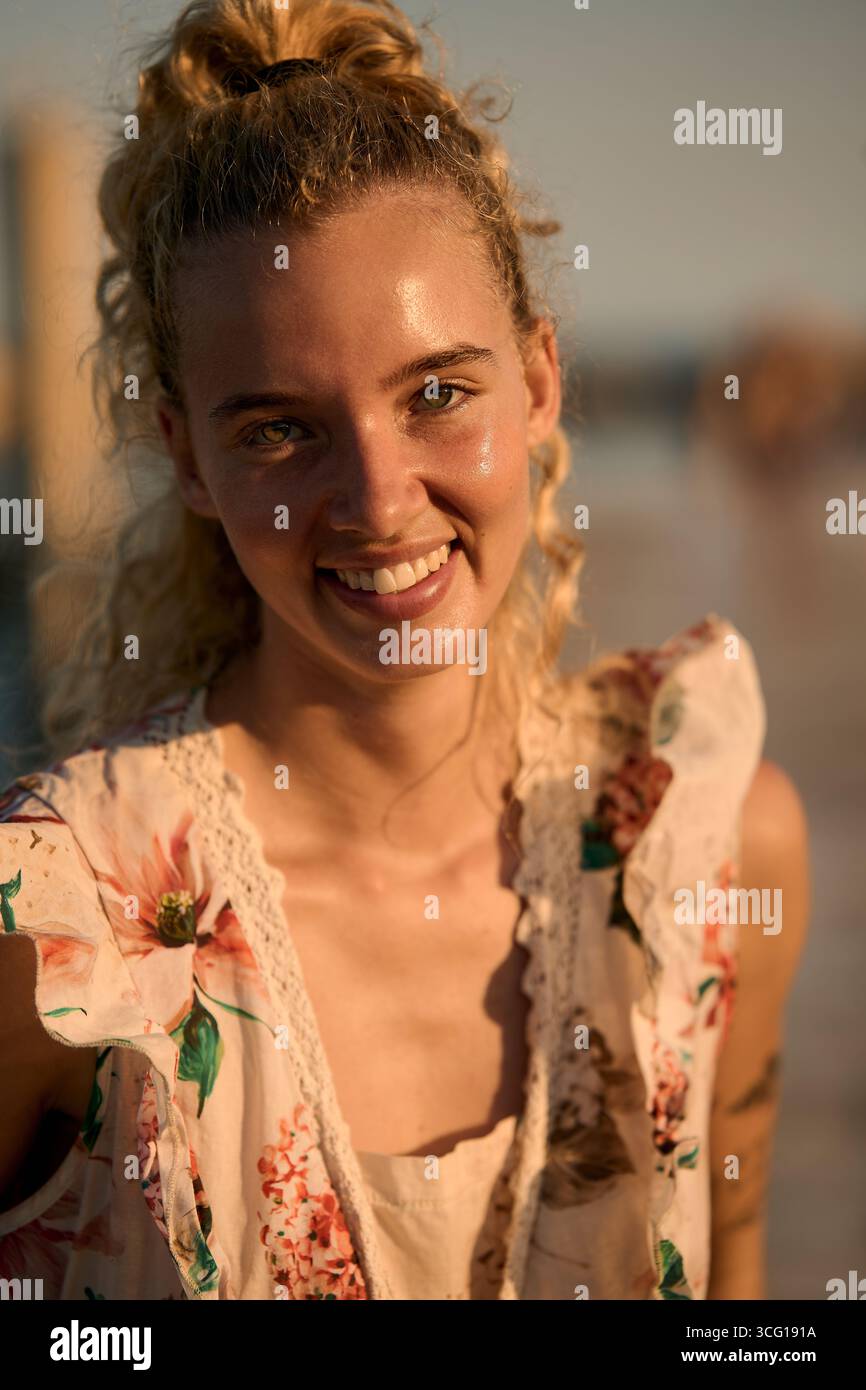 Blonde woman smiling at golden hour on beach Stock Photo