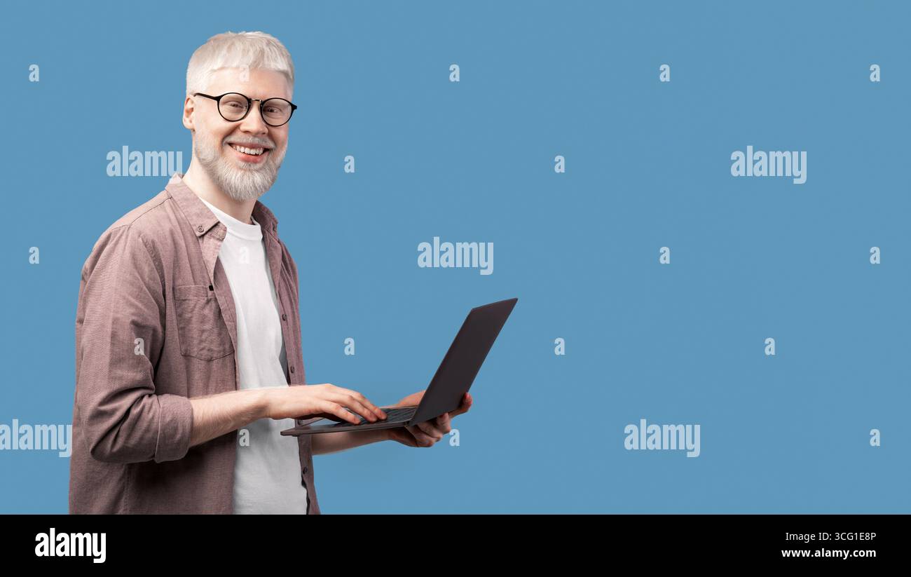 Working with joy. Young albino man using laptop and looking with smile to camera over turquoise studio background Stock Photo