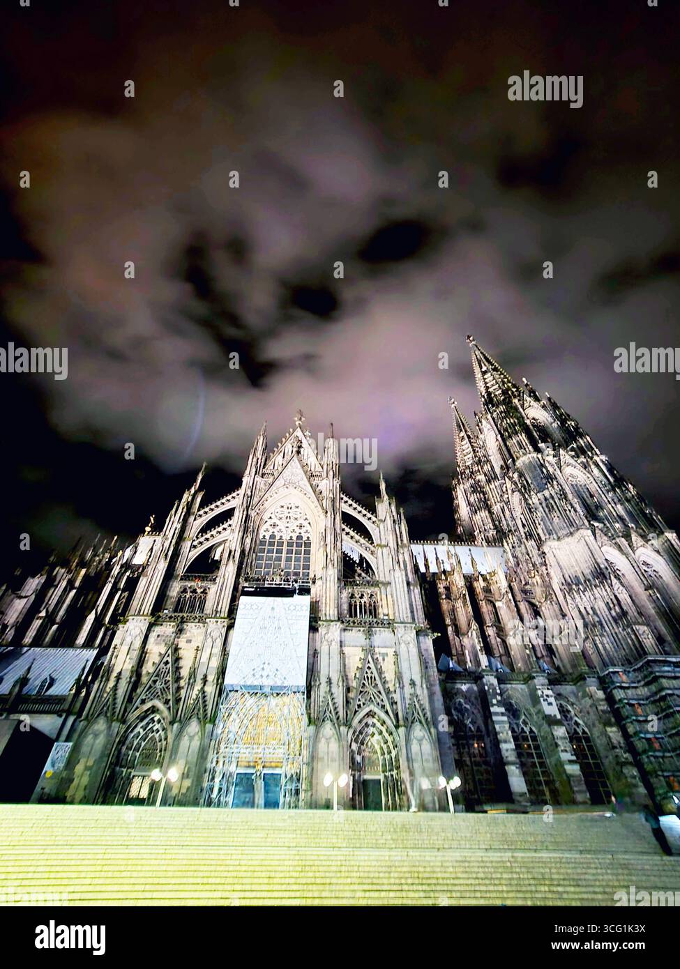 Cologne Cathedral (Kölner Dom) illuminated at night beneath dramatic clouds, Cologne, North Rhine-Westphalia, Germany. - Smartphone Captured Stock Image