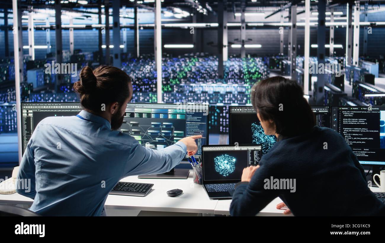 Data center admins doing brainstorming, working on neural network software development. Server farm IT employees working together, implementing machine learning technology using PC, camera A Stock Photo
