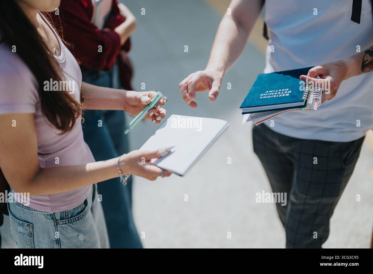 Students collaborating with a professor while reviewing notebooks and taking notes outside Stock Photo