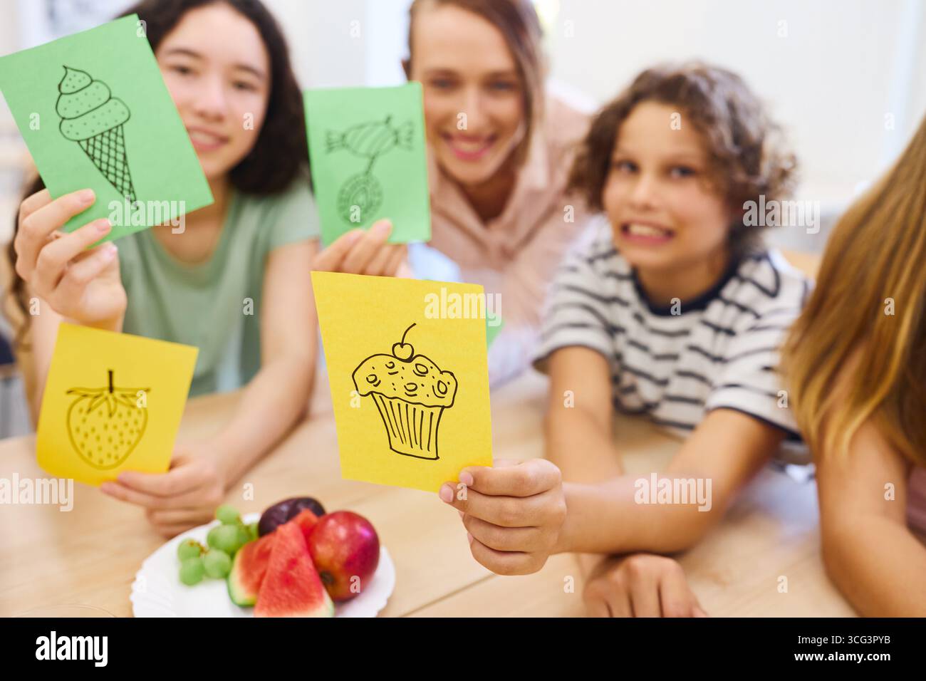 A cheerful group of schoolchildren sharing creative artwork and enjoying natural fresh fruits in a classroom setting, emphasizing learning, fun, and h Stock Photo