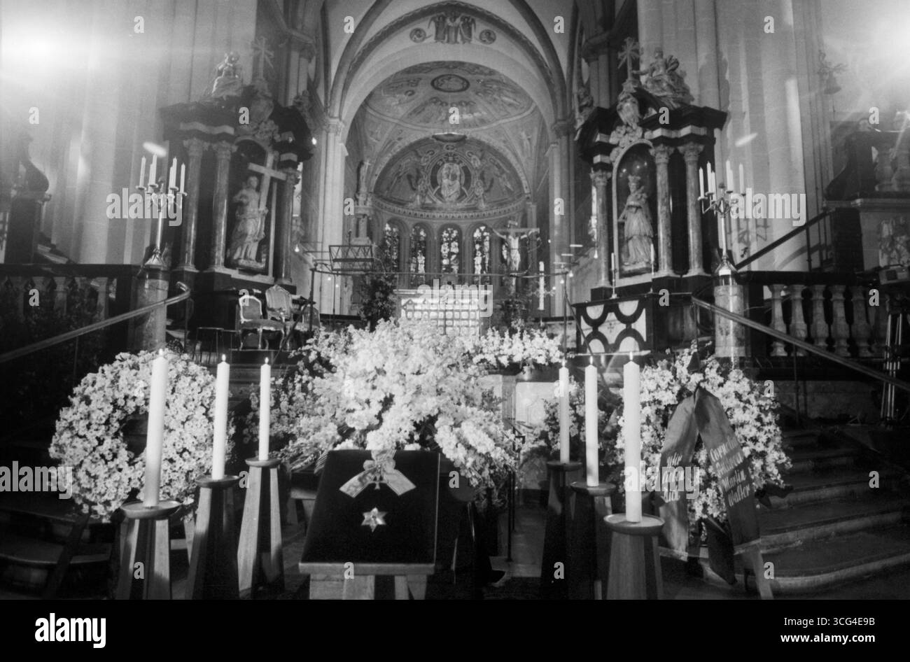 Sarg von Mildred Scheel ist im Bonner Münster feierlich aufgebahrt, umgeben von weißen Blumenkränzen und Kerzen. Im Vordergrund liegt das Bundesverdienstkreuz mit Stern auf Samt. Der festlich geschmückte Altarraum bildet den Hintergrund dieser zentralen Szene des Trauergottesdienstes. Stock Photo