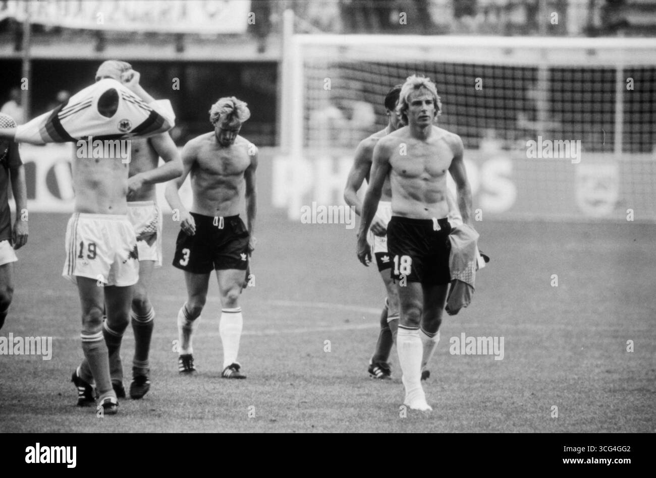 Jürgen Klinsmann (Trikotnummer 18) und seine Mitspieler gehen nach dem Viertelfinalsieg der Fußball-WM 1990 gegen die Tschechoslowakei erschöpft, teils oberkörperfrei, vom Platz. Stock Photo