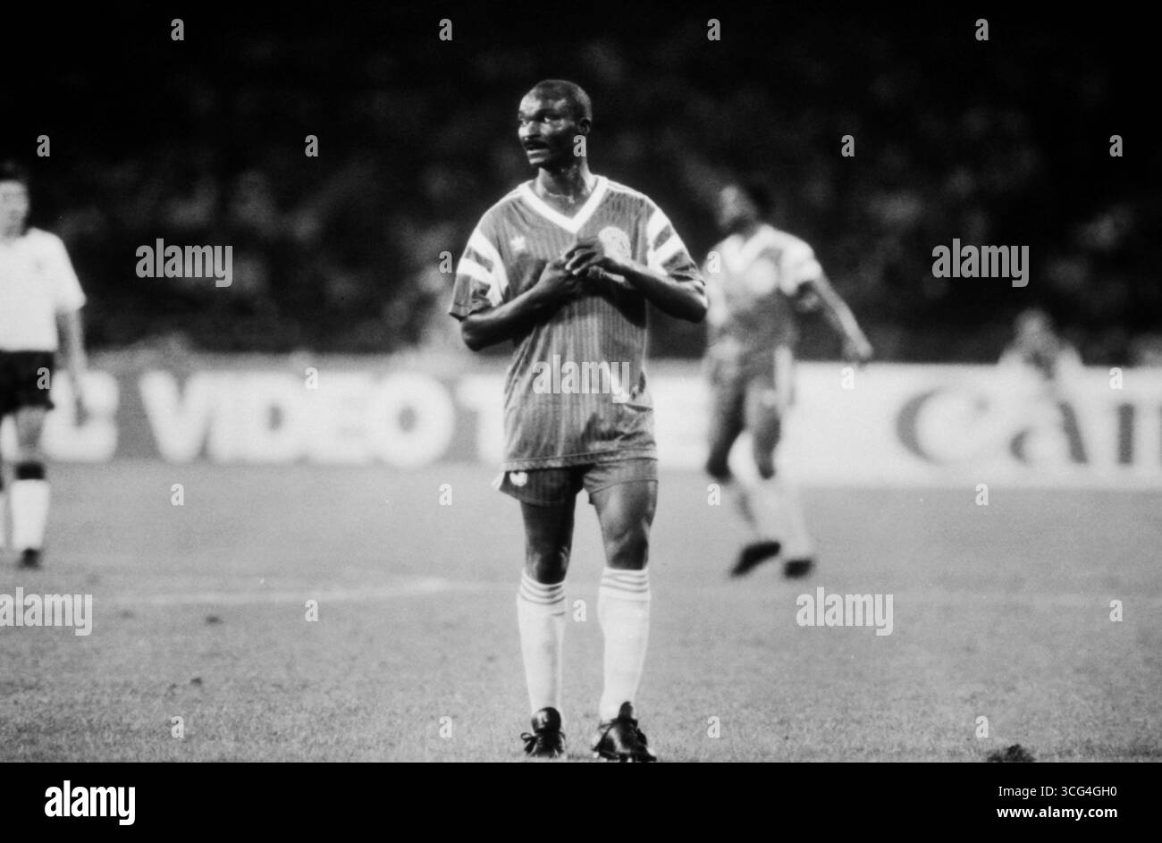 Roger Milla steht auf dem Spielfeld im WM-Viertelfinale 1990 gegen England. Der kamerunische Stürmer blickt konzentriert zur Seite, die Hände an die Brust gelegt. Stock Photo