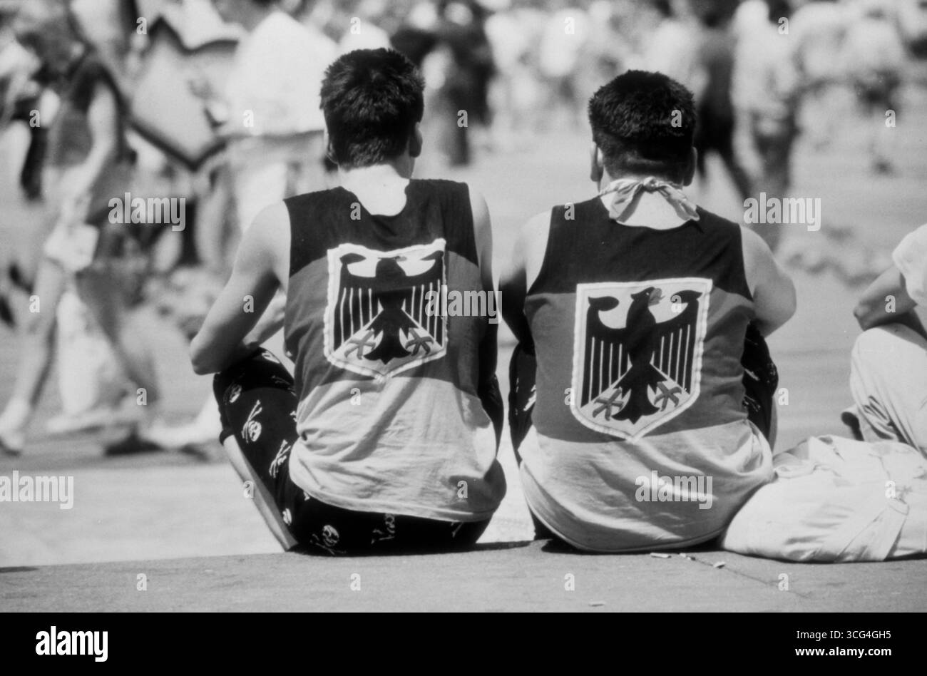 Zwei deutsche Fußballfans von hinten, beide tragen Fan-Shirts in Schwarz-Rot-Gold mit Bundesadler. Die Szene spielt sich im Sommer 1990 während des Viertelfinales der Fußball-Weltmeisterschaft am Mailänder Dom ab. Stock Photo
