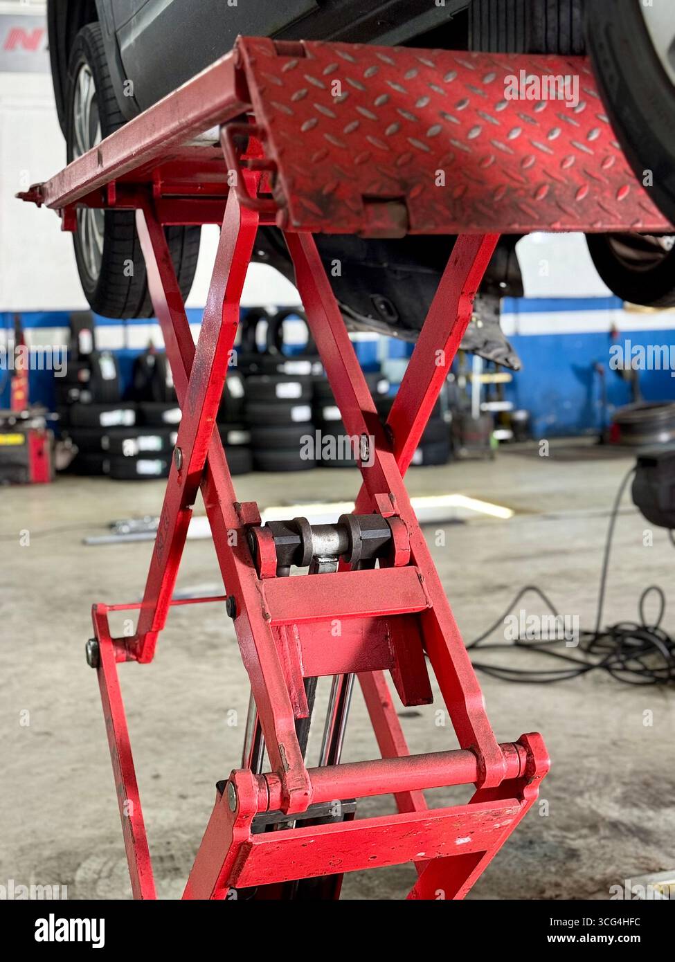 Red hydraulic car lift raising a vehicle inside an automotive repair workshop. - Smartphone Captured Stock Image