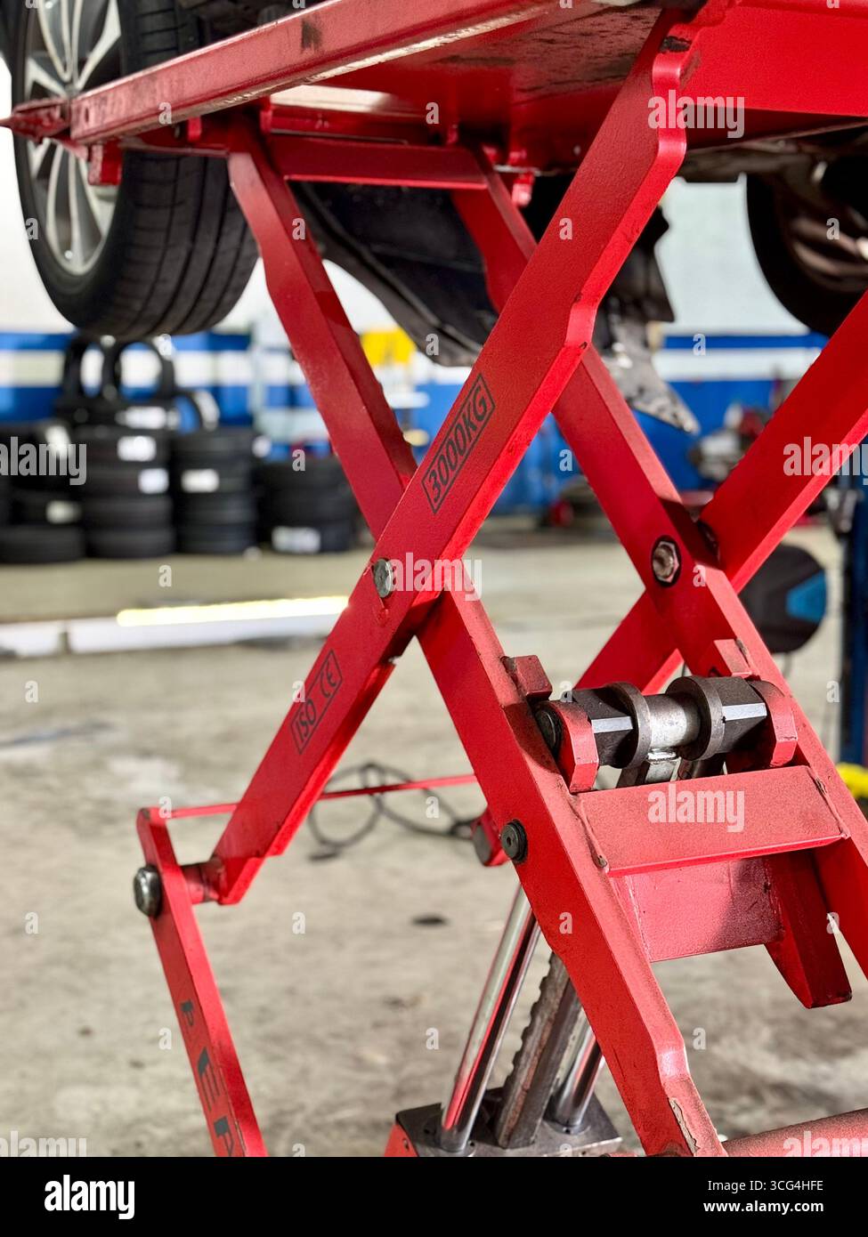 Red hydraulic car lift raising a vehicle inside an automotive repair workshop. - Smartphone Captured Stock Image