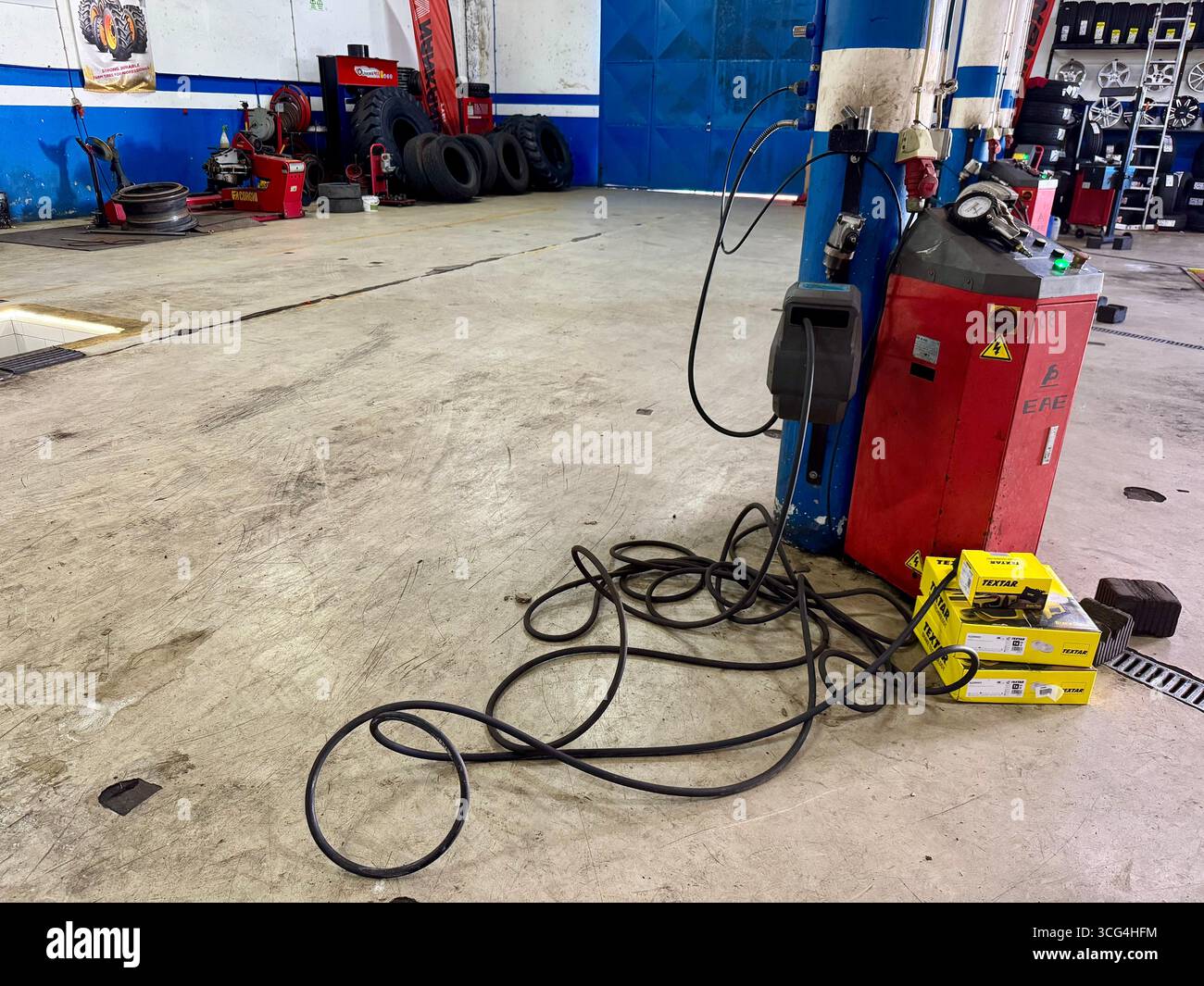 Automotive repair shop interior with equipment, cables, and spare parts on the floor. - Smartphone Captured Stock Image
