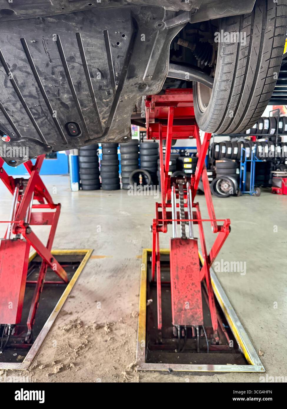 Undercarriage view of a car elevated on red hydraulic lifts inside an automotive repair garage. - Smartphone Captured Stock Image
