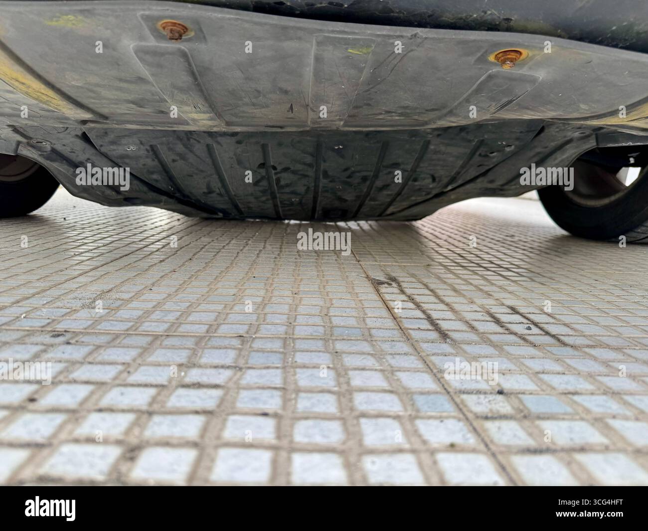 Close-up of a car’s broken or damaged undercarriage resting on a tiled floor. - Smartphone Captured Stock Image