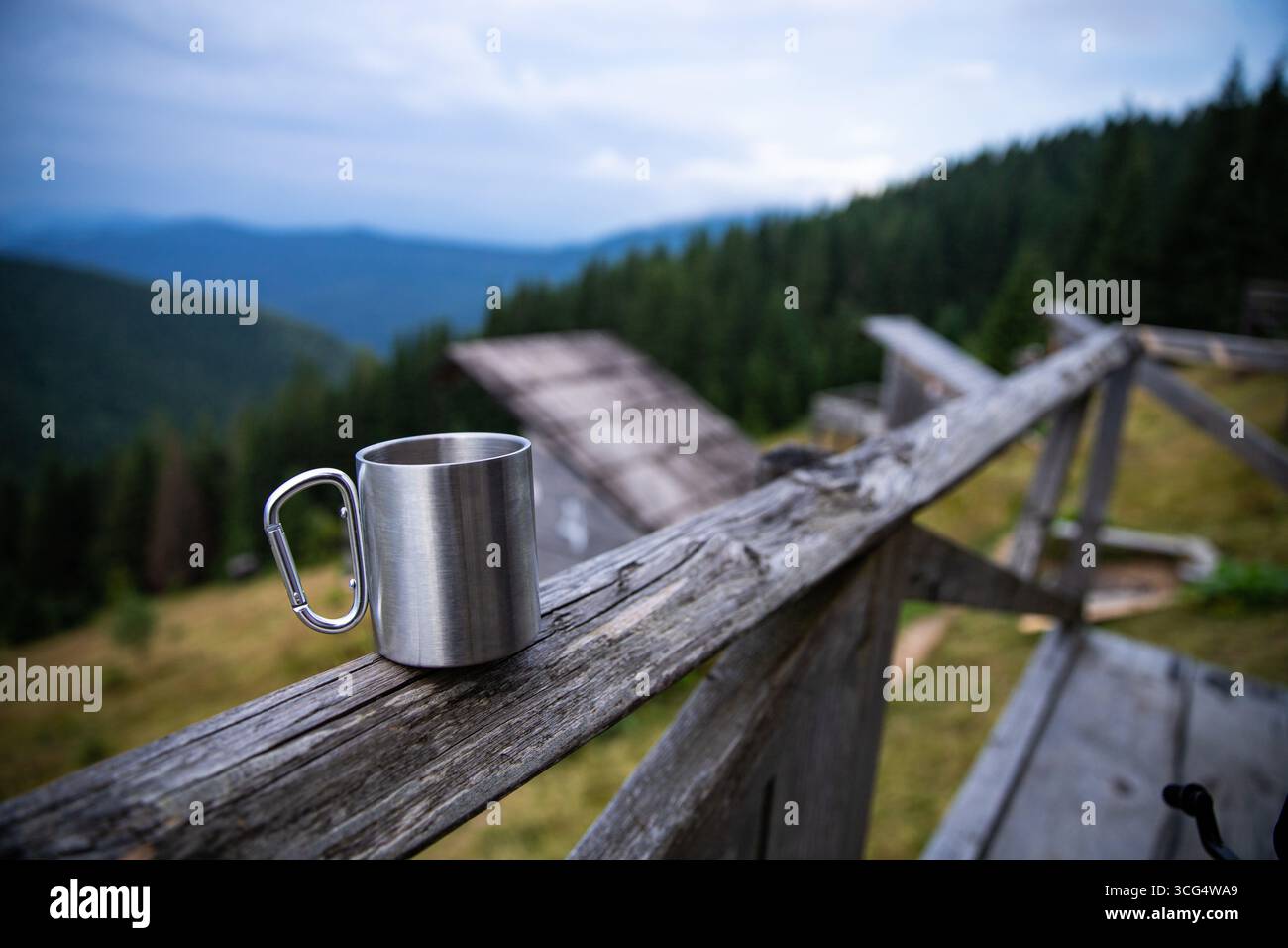 Metal mug with carabiner handle, berries and walnut on rustic fence against scenic mountain background. Travel lifestyle, hiking, camping and enjoying Stock Photo