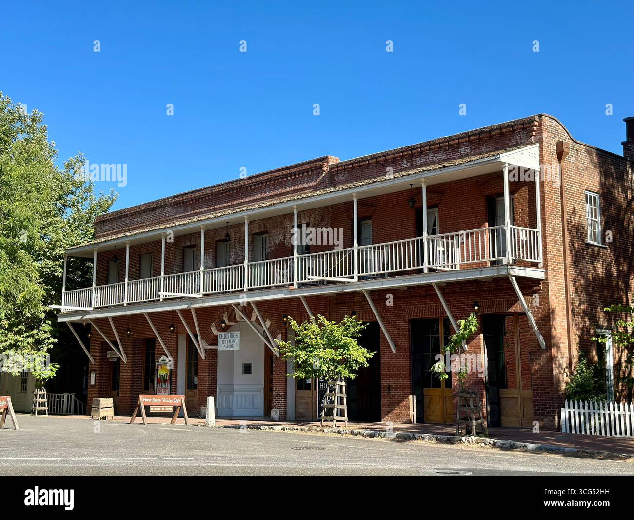 The historic Fallon Hotel, a two-story red brick building with a prominent wooden balcony, stands under a clear blue sky in California - Smartphone Captured Stock Image