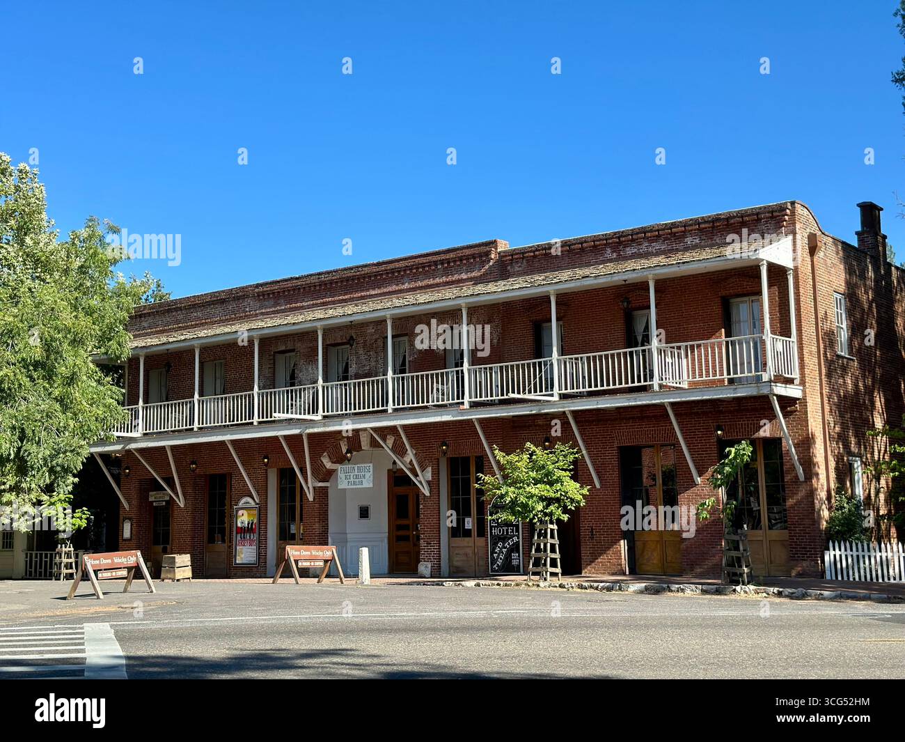The historic Fallon Hotel, a two-story red brick building with a prominent wooden balcony, stands under a clear blue sky in California - Smartphone Captured Stock Image