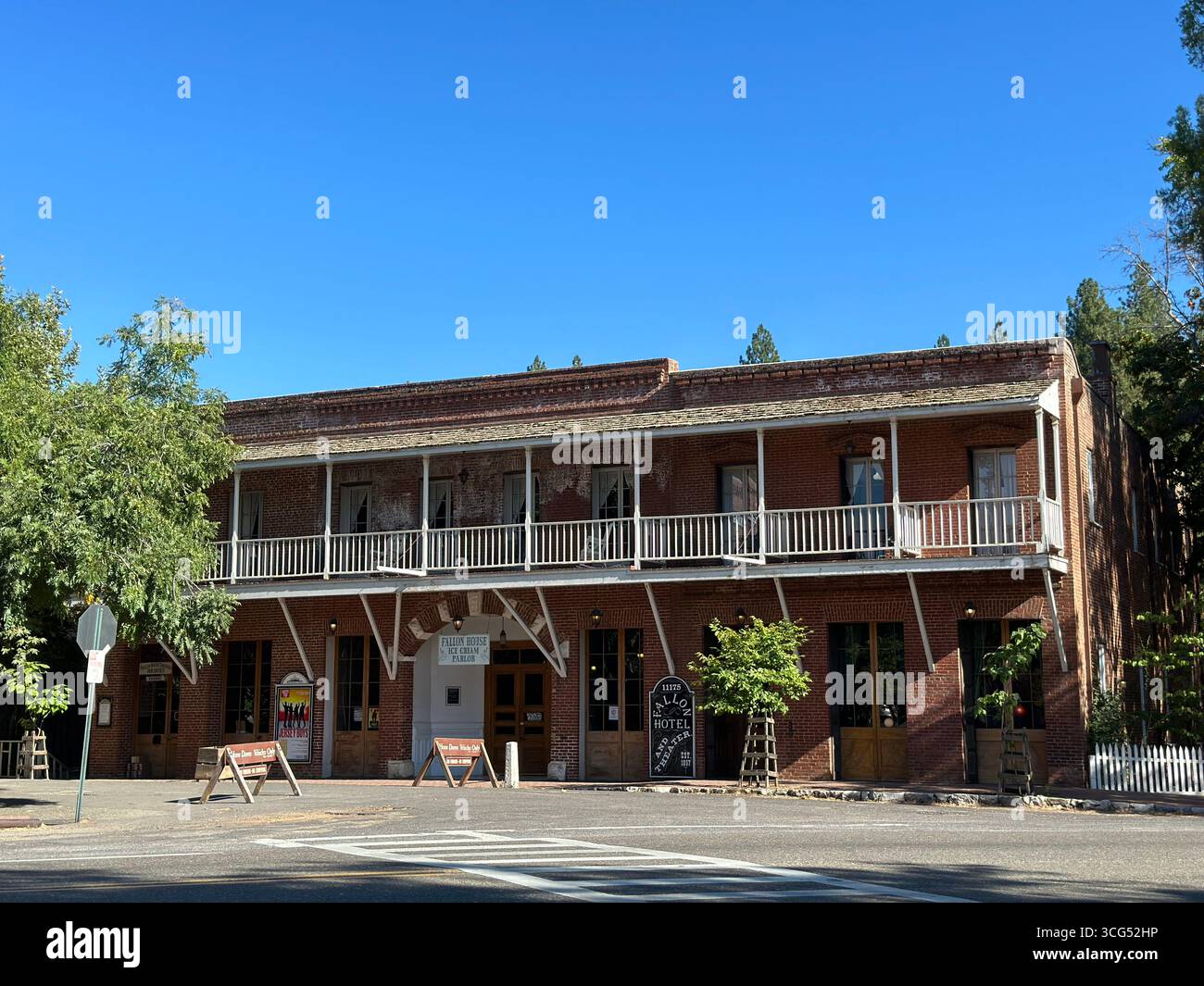 The historic Fallon Hotel, a two-story red brick building with a prominent wooden balcony, stands under a clear blue sky in California - Smartphone Captured Stock Image