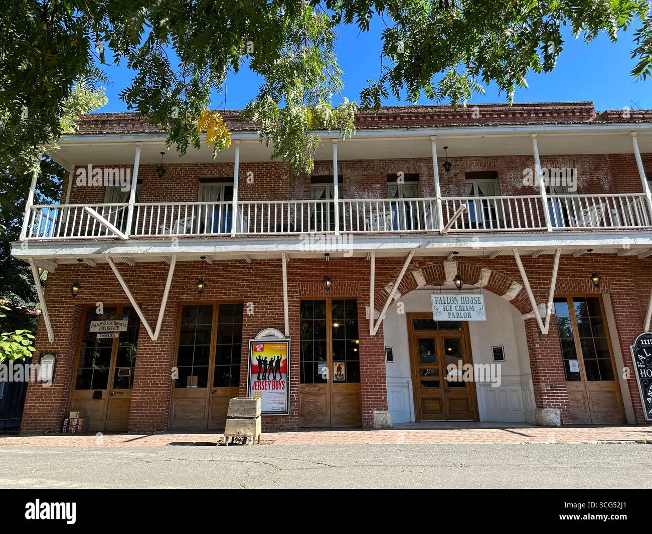 The historic Fallon Hotel, a two-story red brick building with a prominent wooden balcony, stands under a clear blue sky in California - Smartphone Captured Stock Image