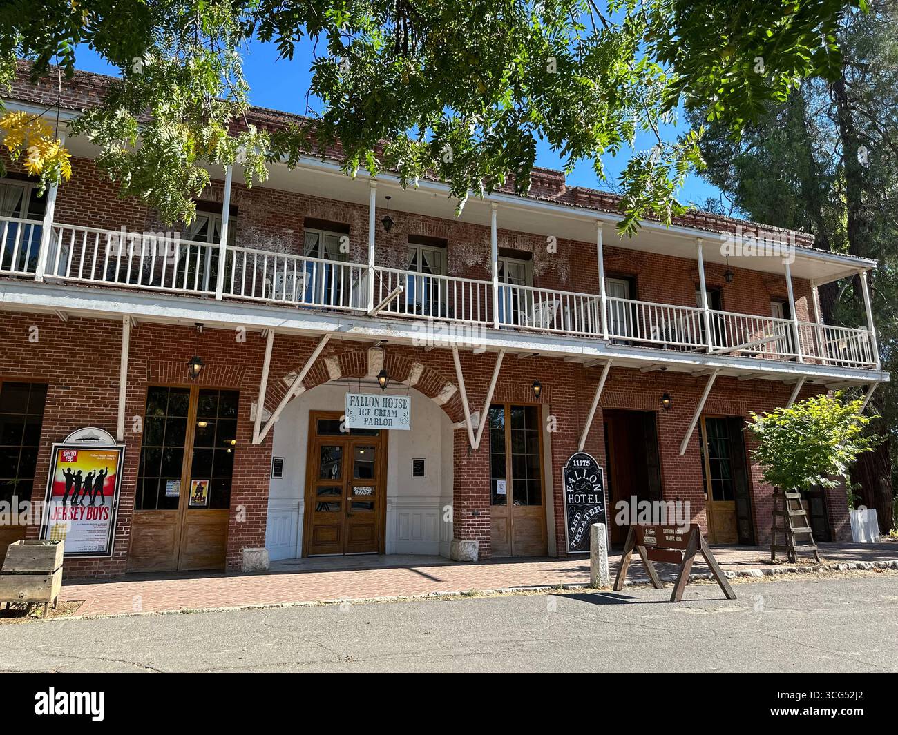 The historic Fallon Hotel, a two-story red brick building with a prominent wooden balcony, stands under a clear blue sky in California - Smartphone Captured Stock Image