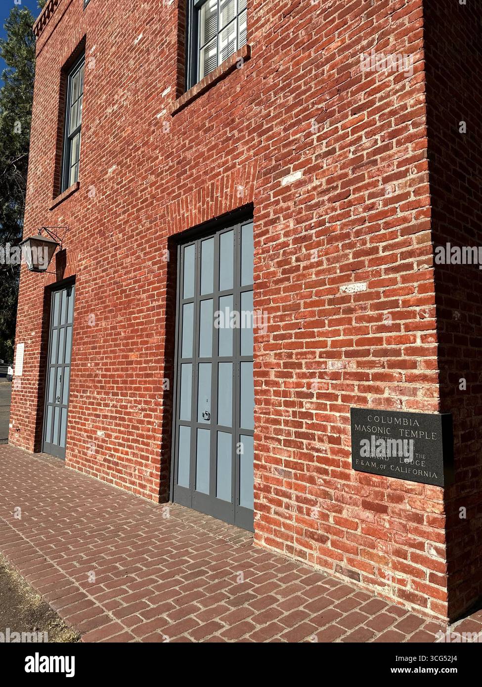A lantern with the Freemason Square and Compass symbol hangs on the exterior of a historic red brick building. - Smartphone Captured Stock Image