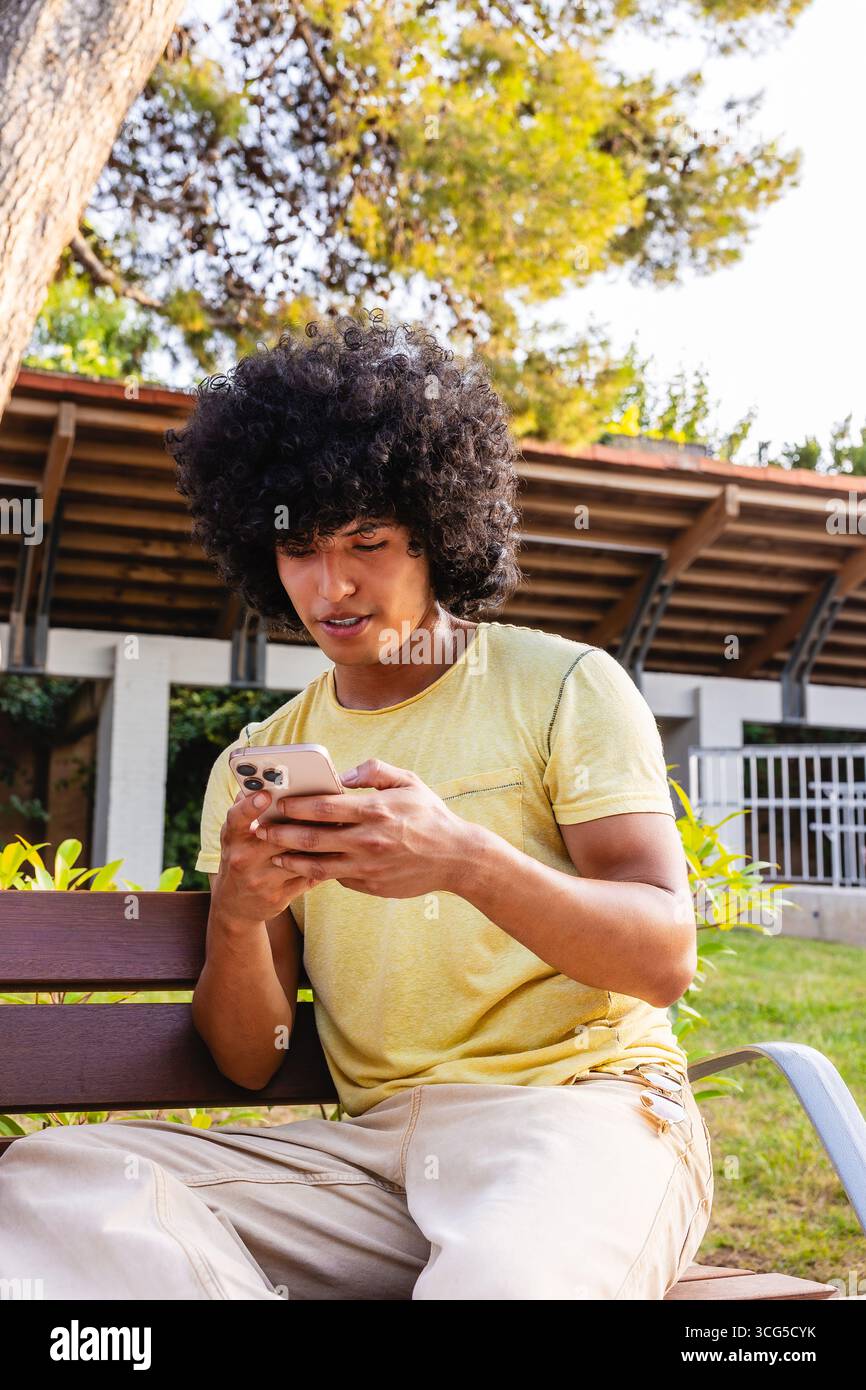 Young man with afro hair using smartphone sitting on bench in a park Stock Photo