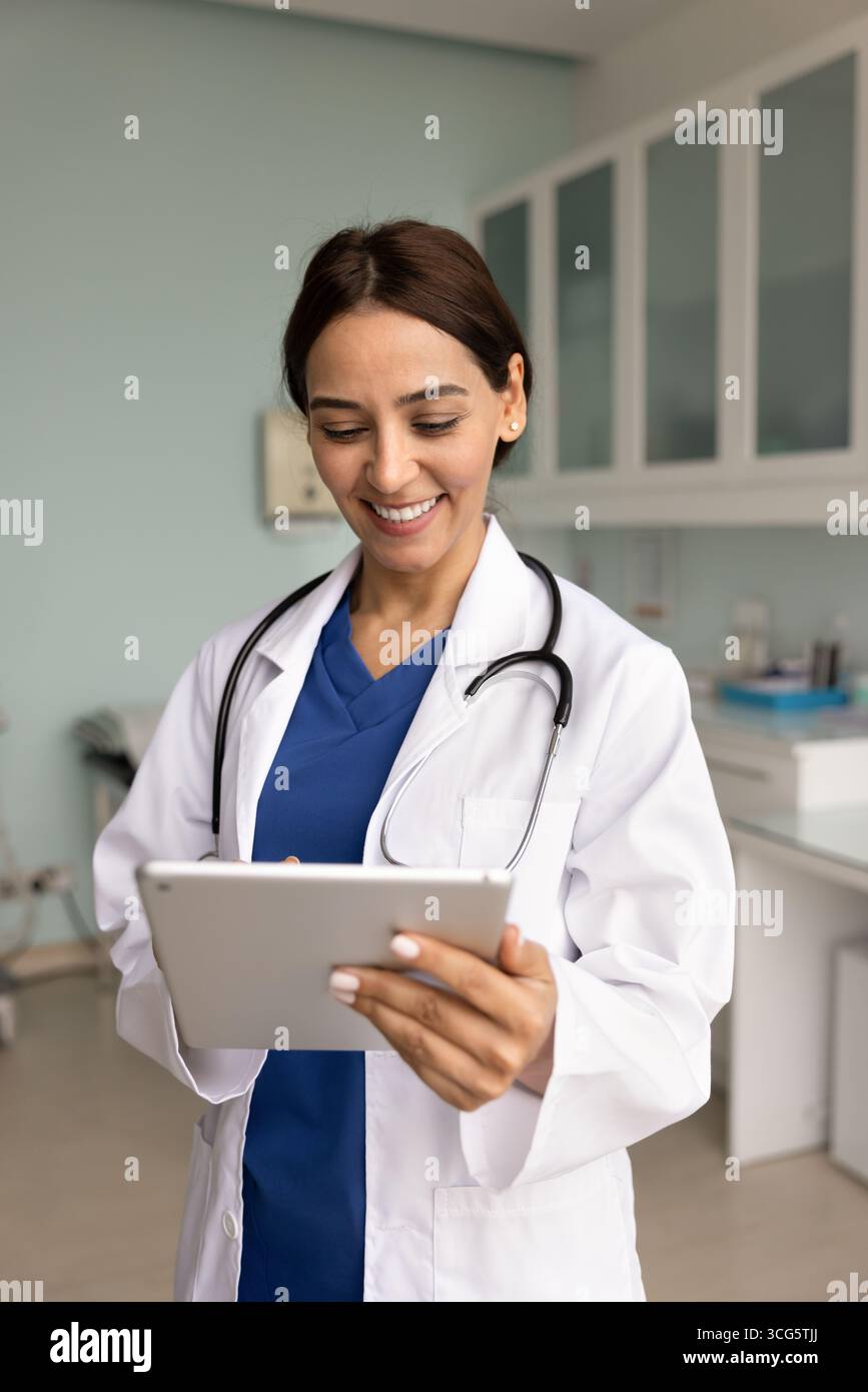 Happy young 30s doctor woman in lab coat using tablet Stock Photo