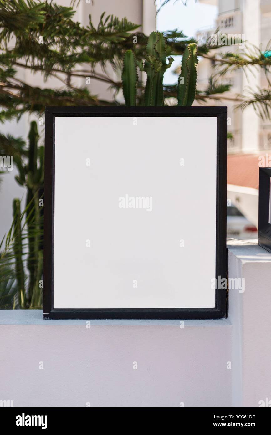A blank sign rests on a ledge surrounded by lush greenery. Bright ...