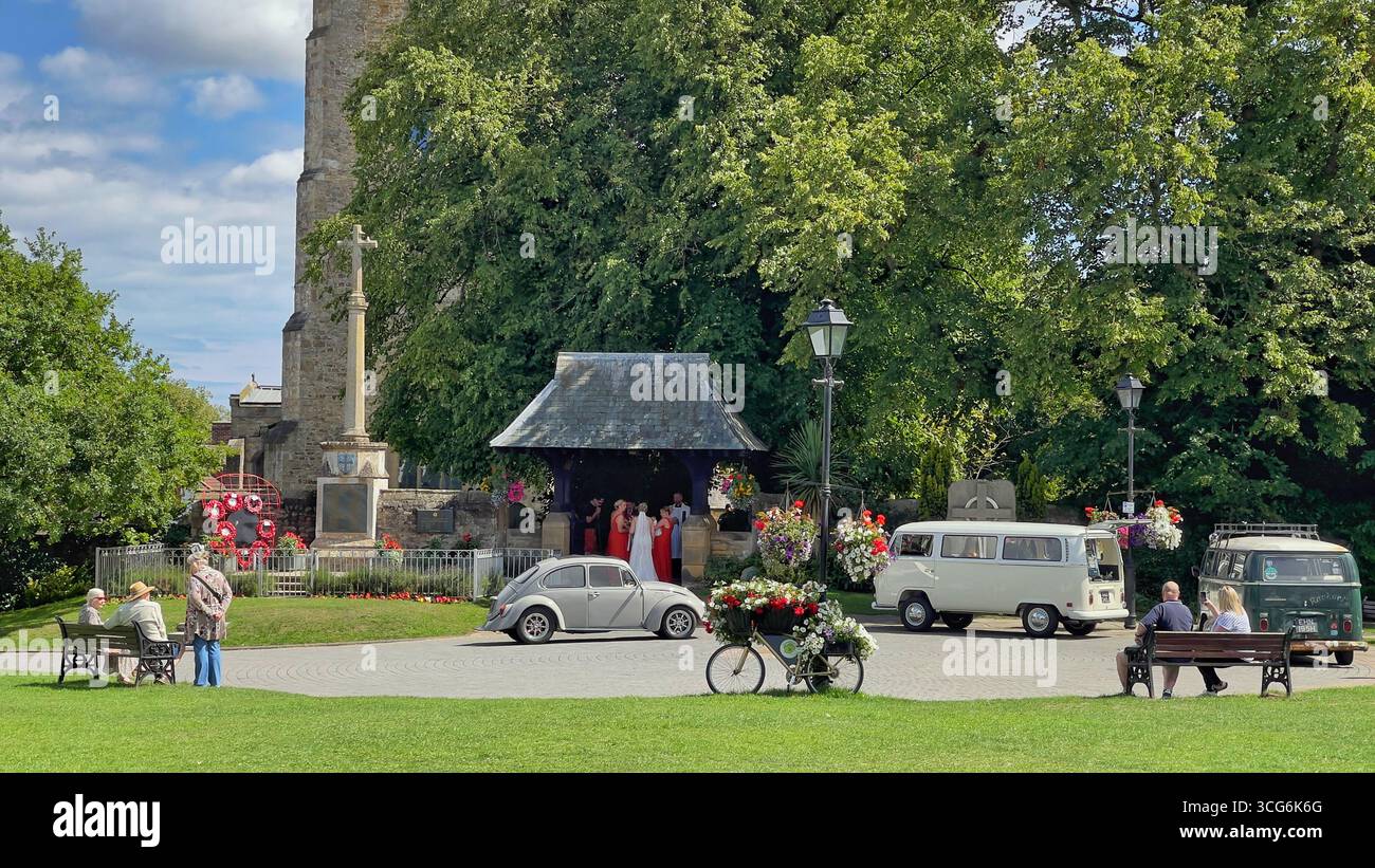 A vintage white Volkswagen Beetle adds charm to a wedding scene in Sedgefield, UK, set against a historic church and formal gathering Stock Photo