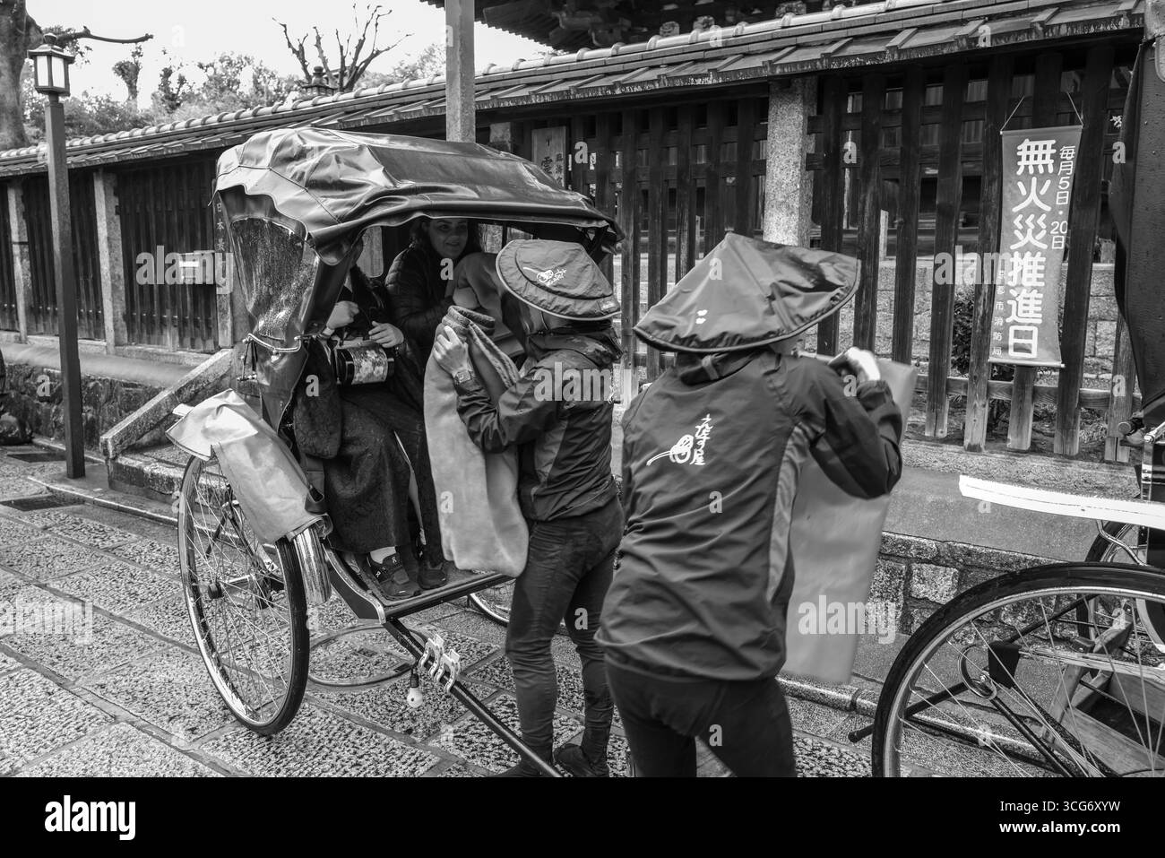 Black and white photograph of local people in a traditional Japanese rickshaw on a rainy street, Yasaka Kamimachi, Higashiyama Ward, Kyoto, Kansai, Ho Stock Photo