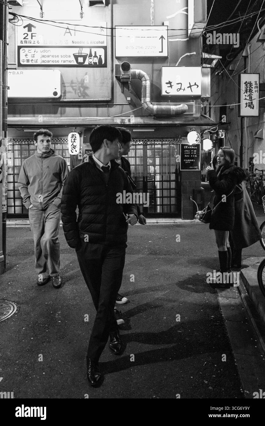A dynamic black-and-white scene of individuals walking through a lively, atmospheric urban alley, depicting bustling social interactions and cultural Stock Photo