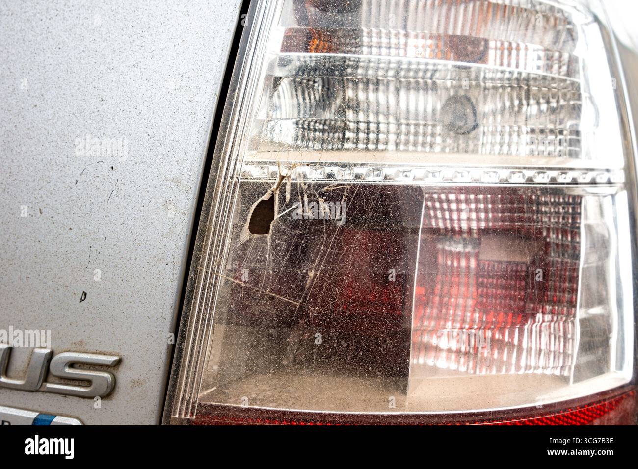 A detailed view of a cracked tail light lens with a central hole and spiderweb-like fractures, showing signs of impact damage and dirt accumulation wi Stock Photo