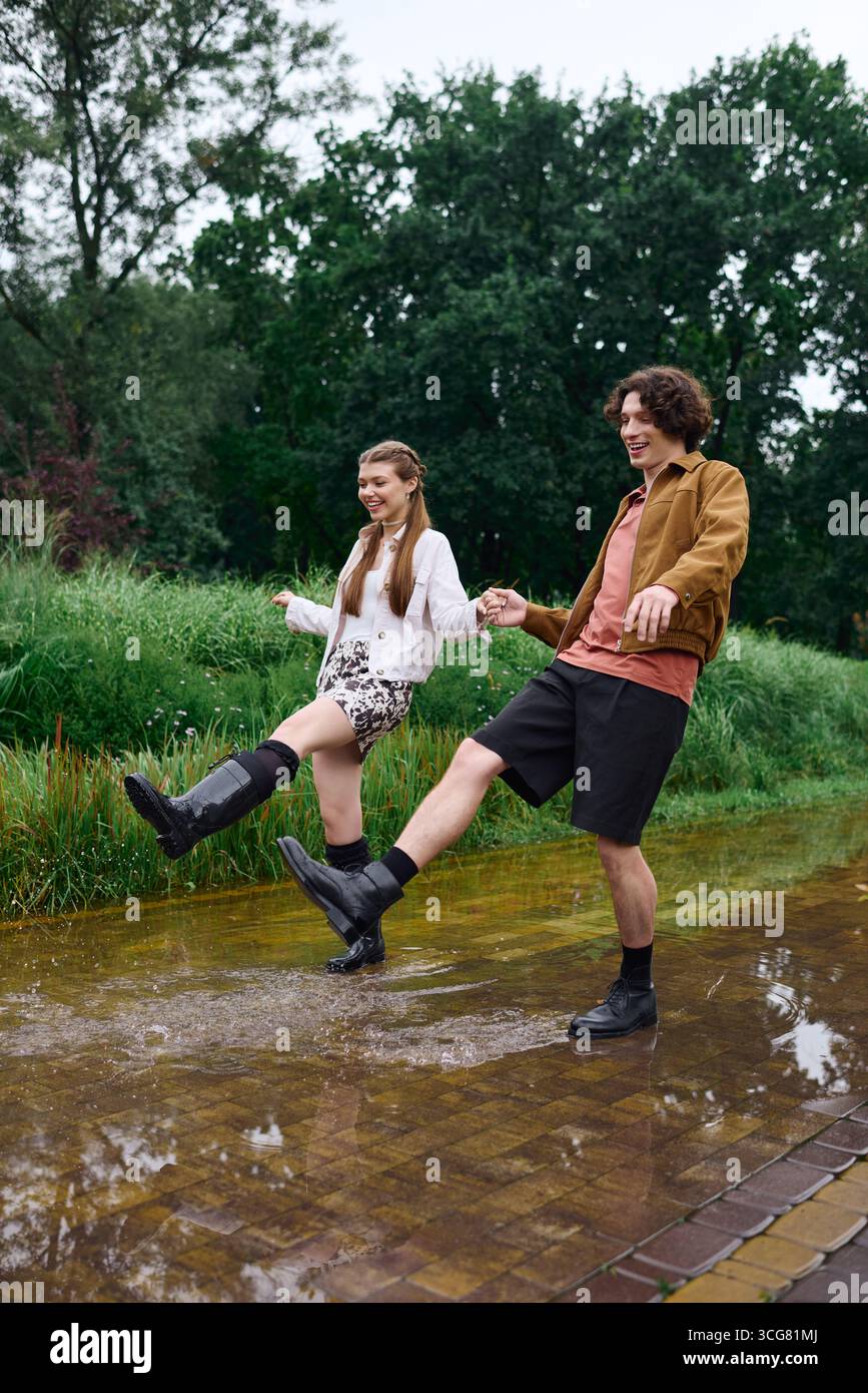 A man and woman stroll through a vibrant park, splashing in puddles and enjoying rainy weather. Stock Photo