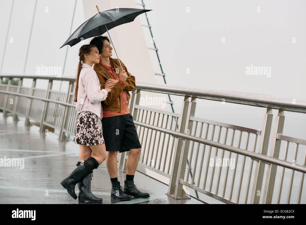 A loving couple enjoys their time together, sharing an umbrella and laughter during a rainy stroll. Stock Photo