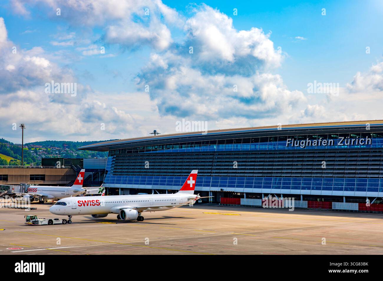 Zurich Airport and Main Building and Swiss Airlines Passenger Airplane on Airfield in a Sunny Summer Day with Blue Sky and Clouds From the Airport in Stock Photo