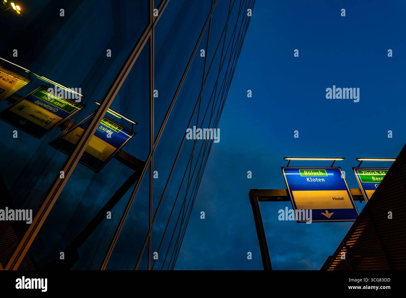 Modern Glass Building with Reflection and Illuminated Road Sign to Zurich Airport at Night in the Airport in Kloten, Zurich, Zurich Canton, Switzerlan Stock Photo