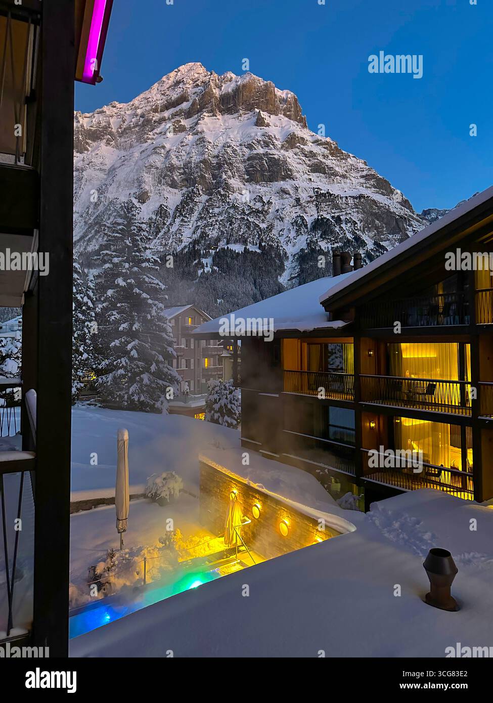 Balcony View with House and Illuminated Outdoor Swimming Pool and Mountain Peak Wetterhorn in a Snowy Winter Day in Dusk in Grindelwald, Bern Canton, Stock Photo