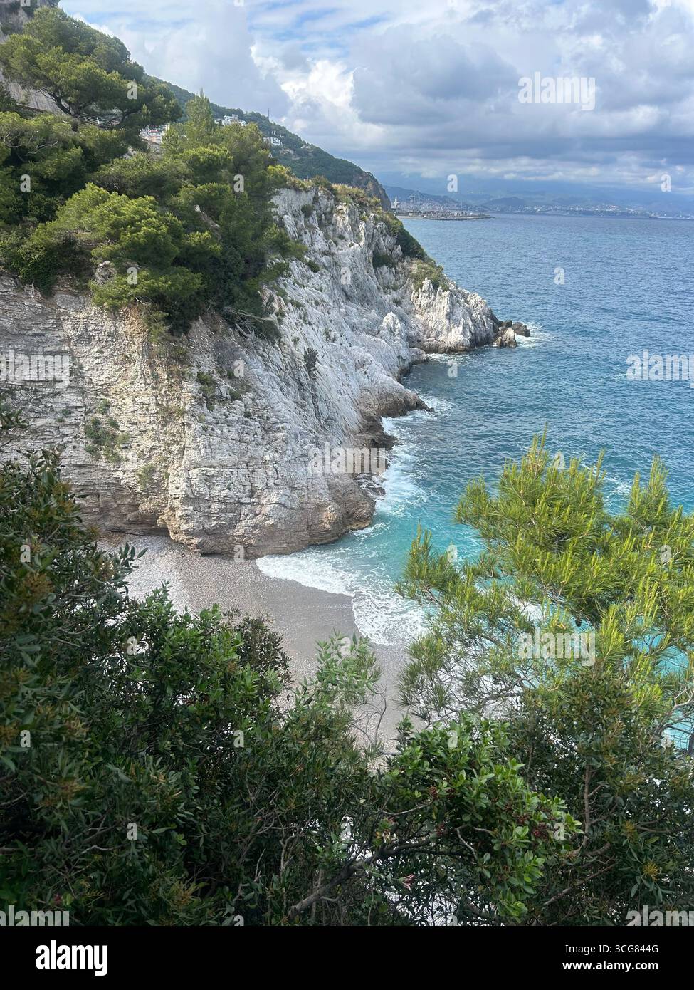 Rocky cliffs with pine trees and a hidden pebble beach along the coastline of Crete, Greece. - Smartphone Captured Stock Image