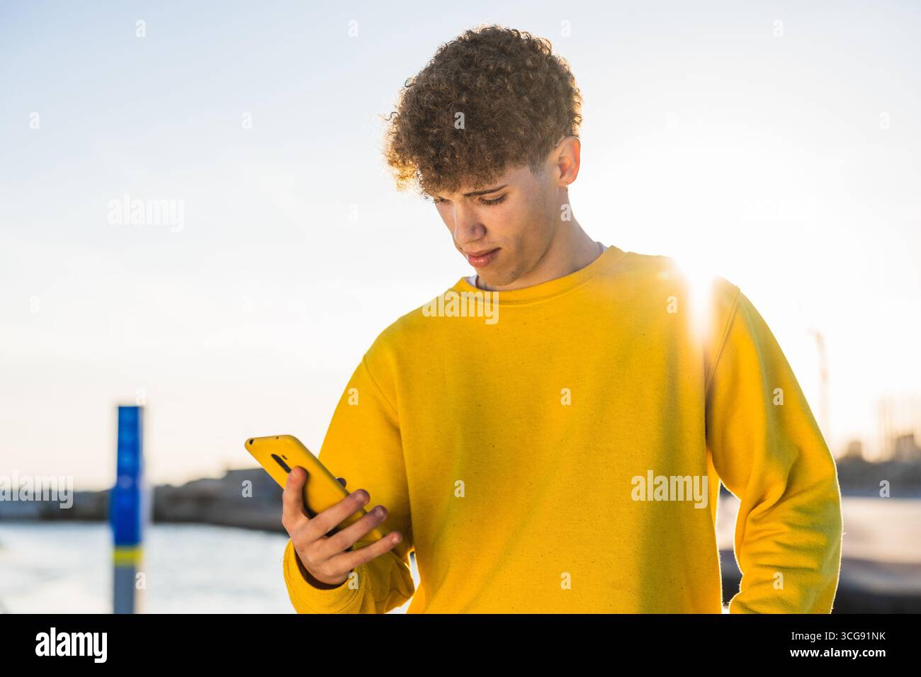 Young man using smartphone by the sea at sunset Stock Photo