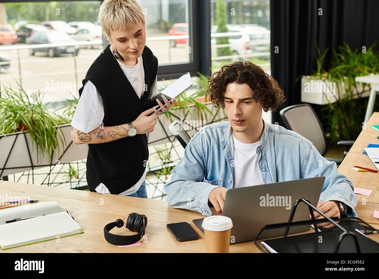 Two young professionals engage in a collaborative work session, sharing ideas and tools. Stock Photo