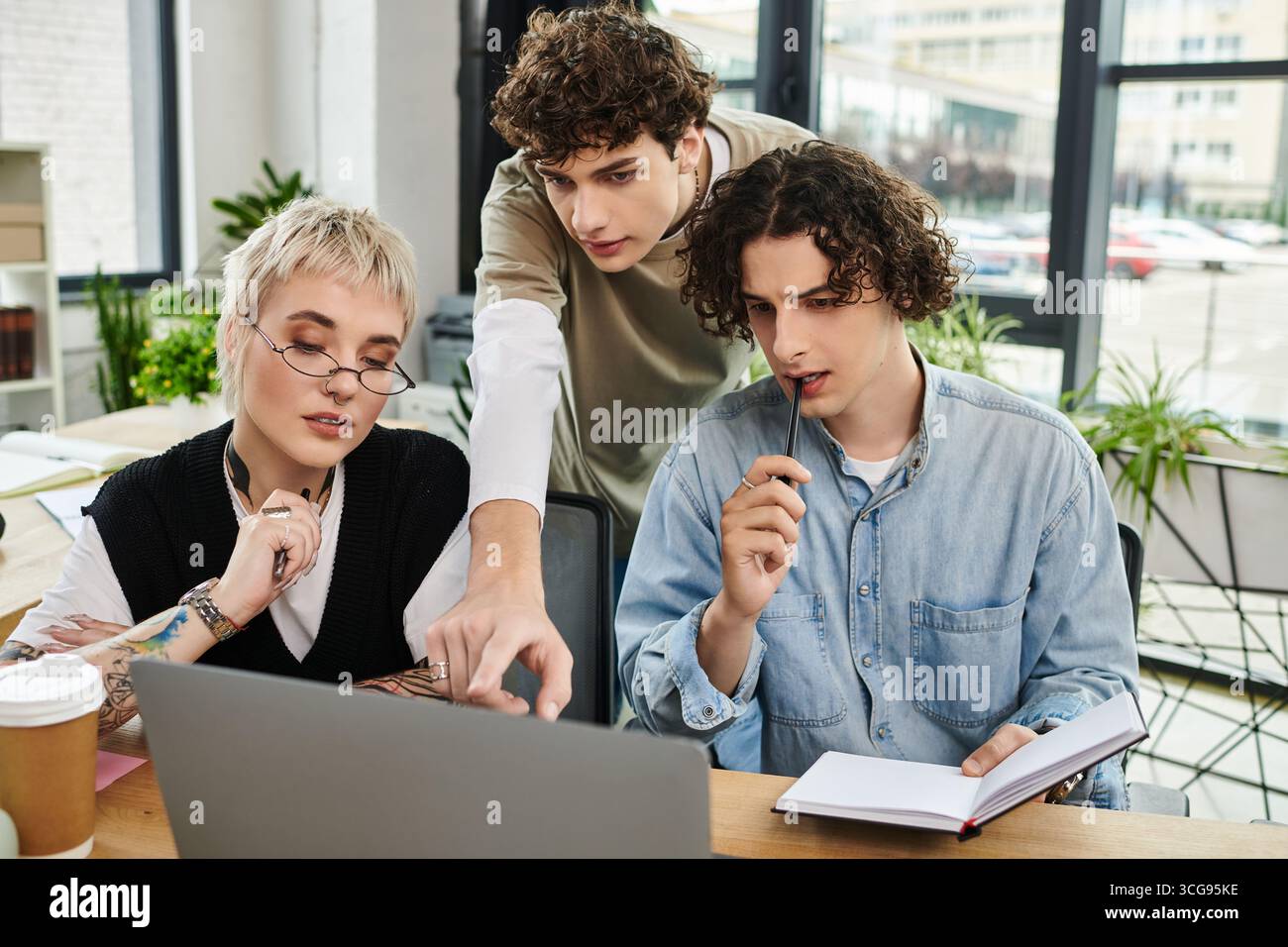 Three young professionals collaborate at a modern office desk, discussing and solving problems. Stock Photo