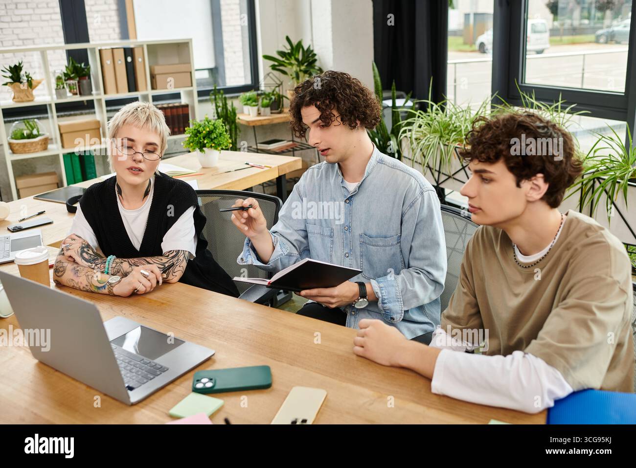 Three young professionals engage in a collaborative discussion at an office workspace. Stock Photo