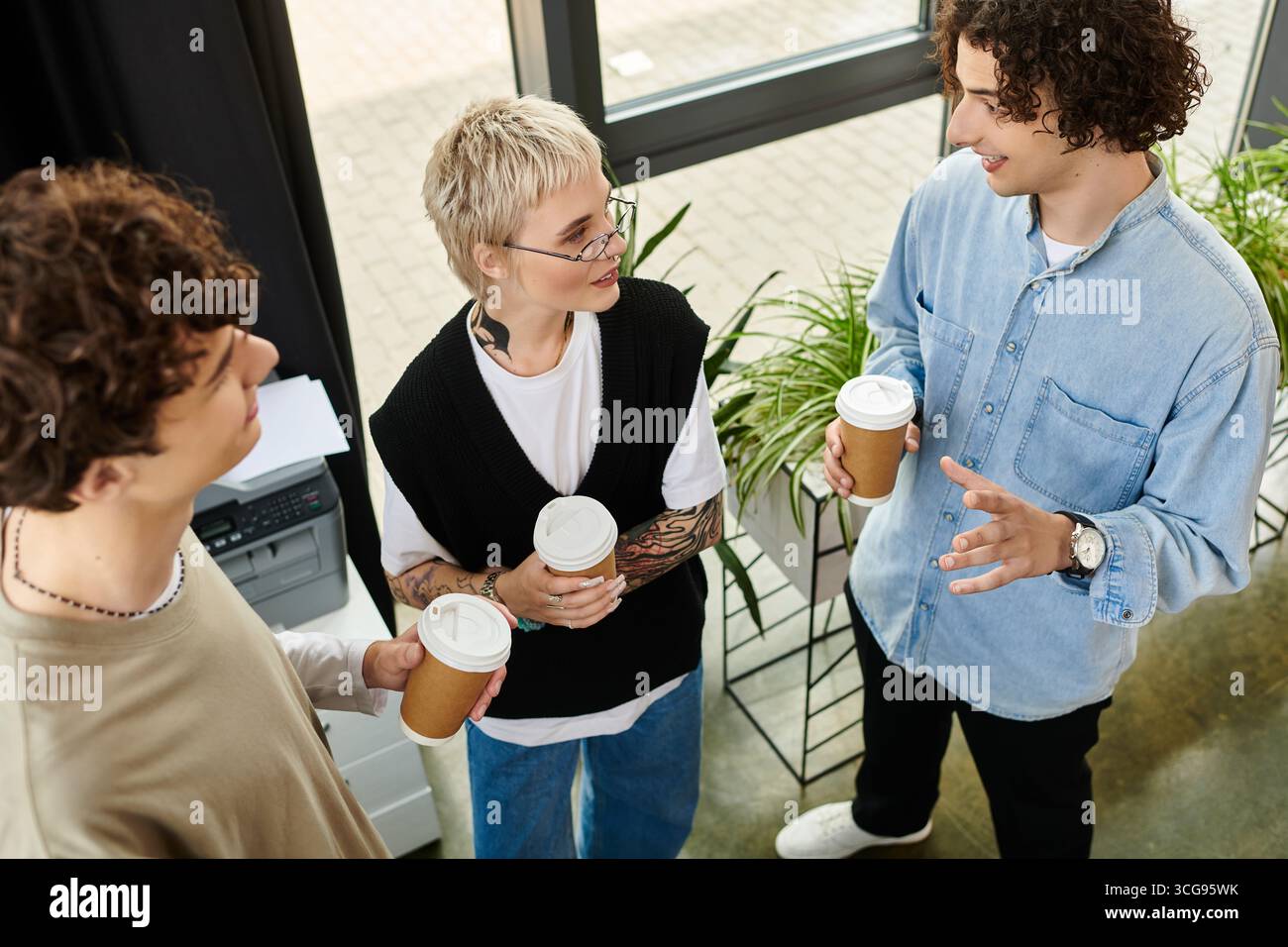 Three young professionals share ideas and enjoy coffee during a productive workday. Stock Photo