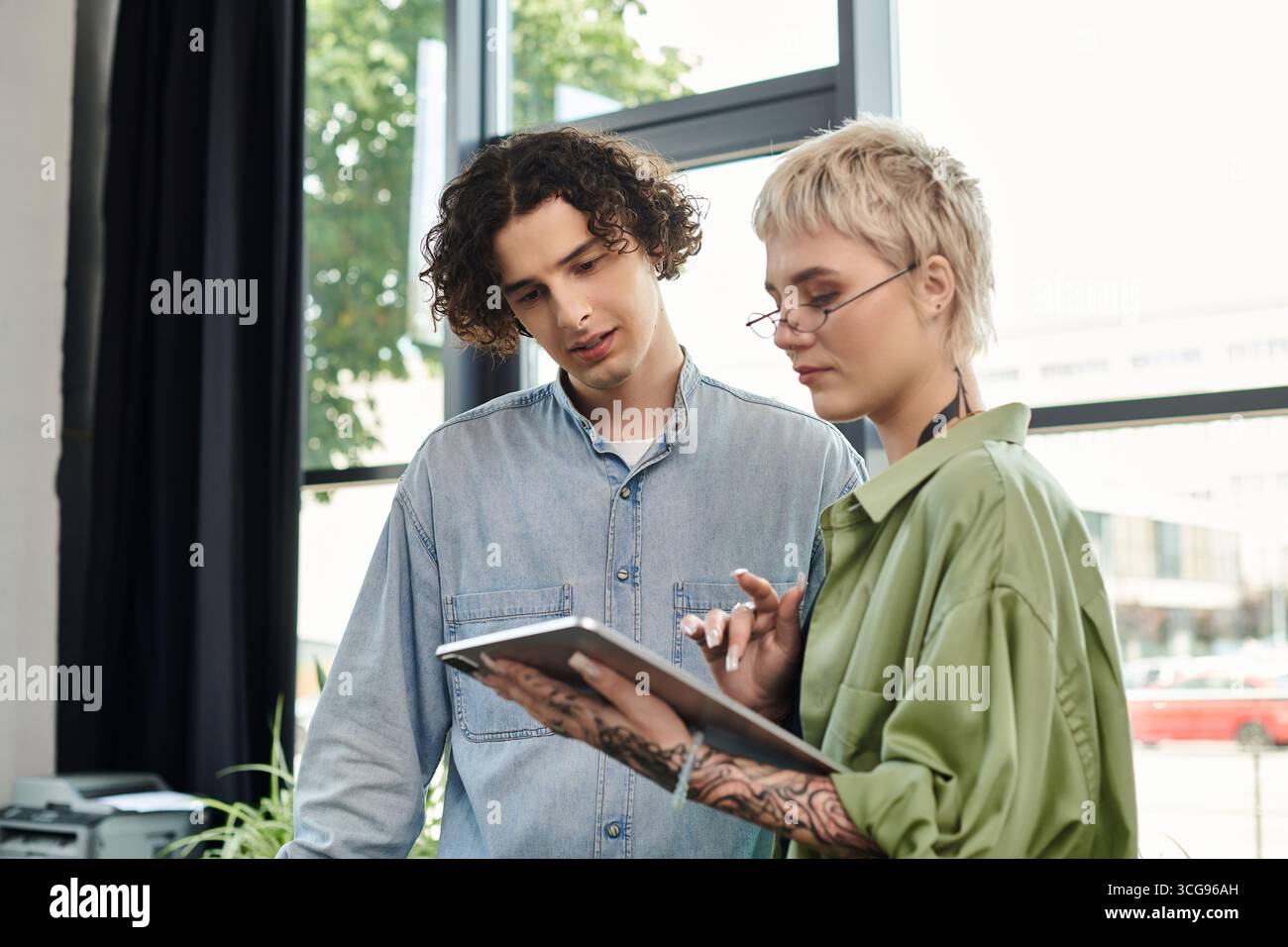 Two young professionals collaborate on a project while discussing ideas and reviewing materials. Stock Photo