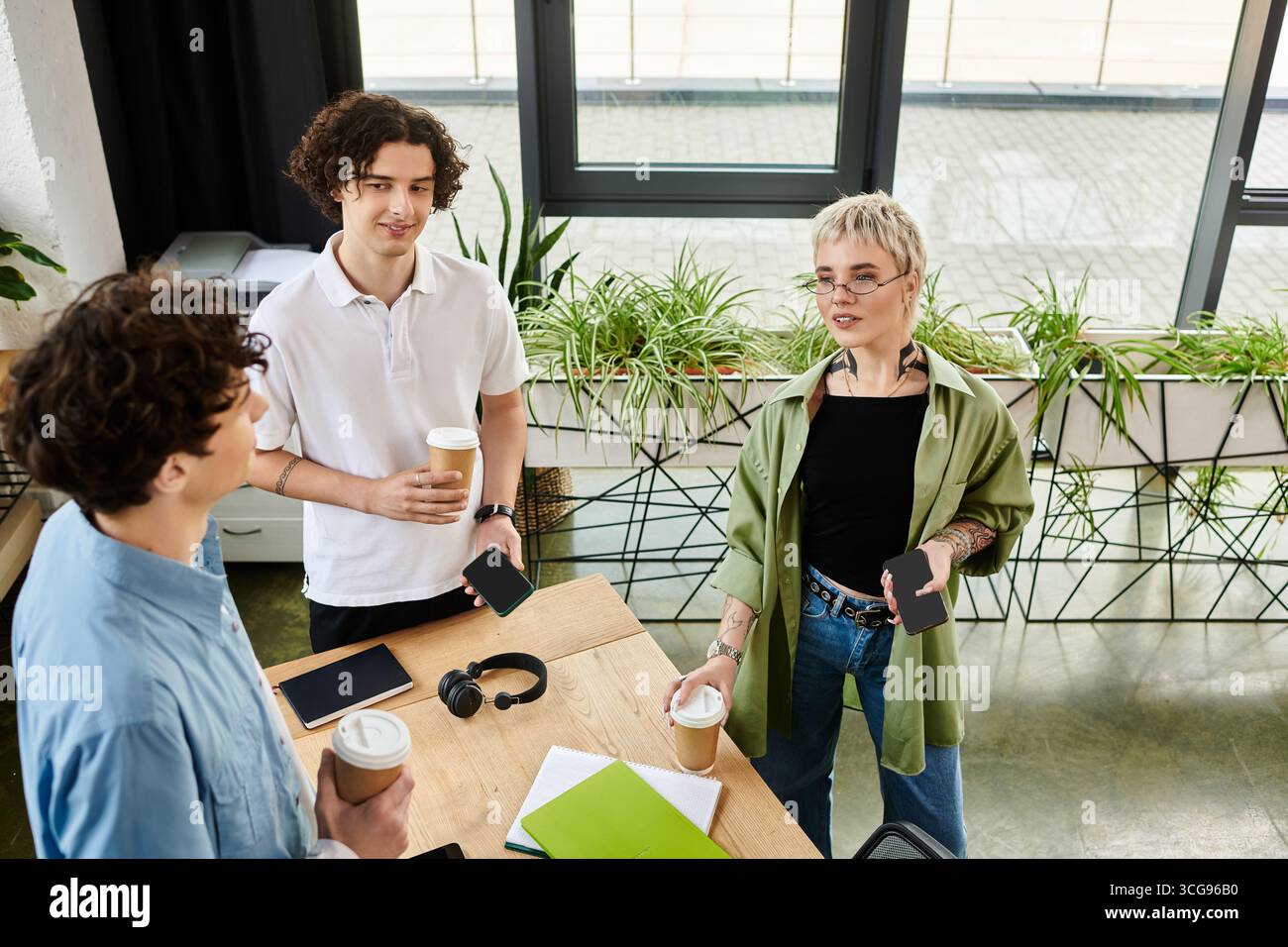Three young workers share ideas over beverages in a vibrant office environment. Stock Photo