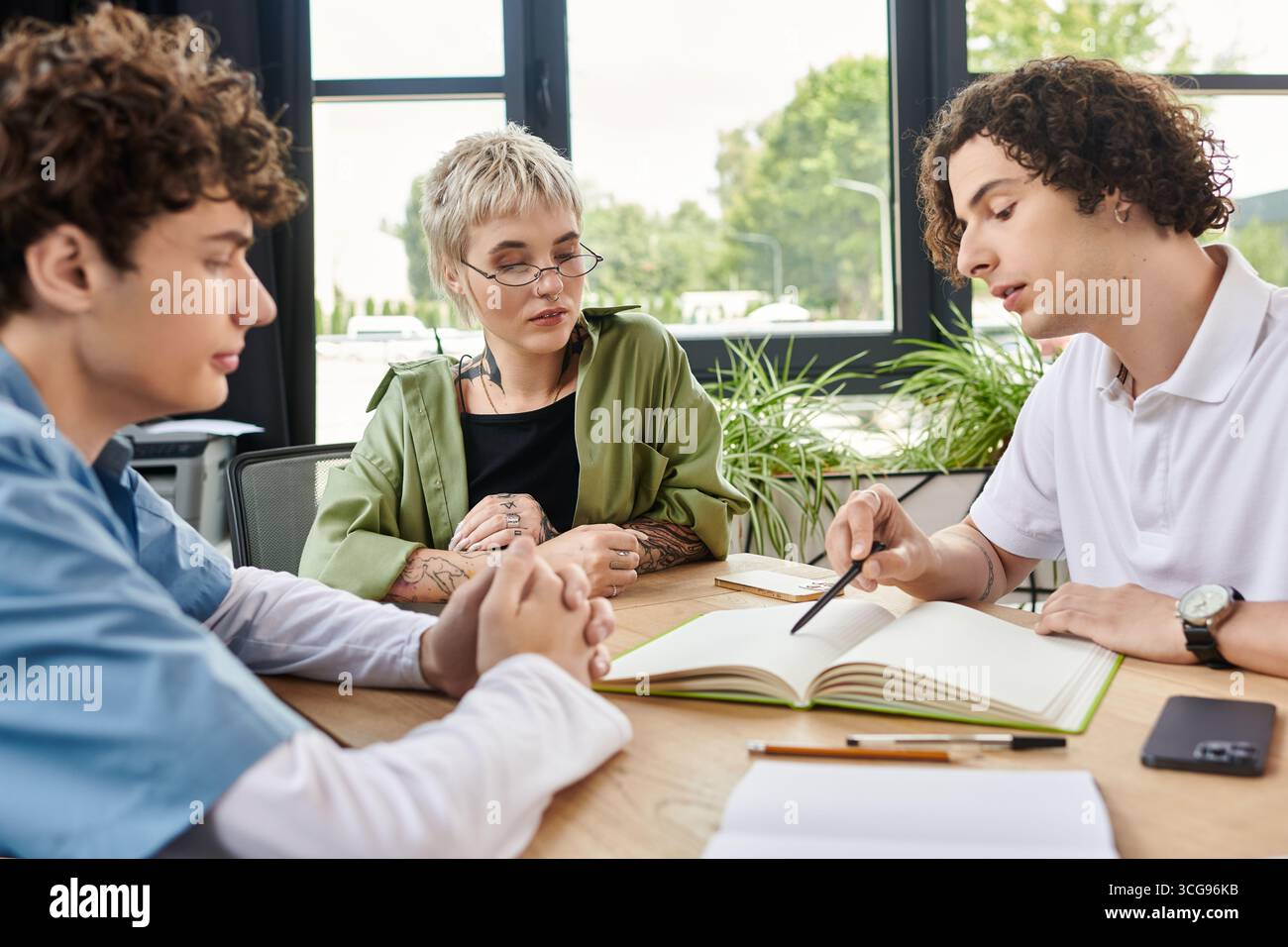 Three young professionals engaged in a discussion while working on a project at a table. Stock Photo